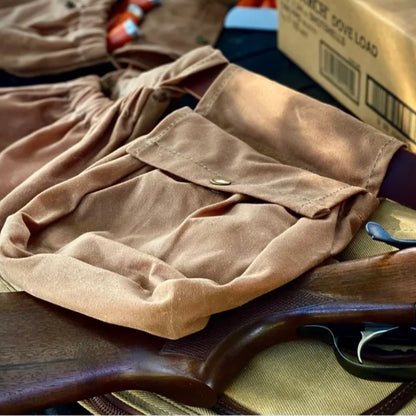 Close-up of a russet brown shotgun shell pouch on a table, showcasing its antique brass snap and elastic opening.