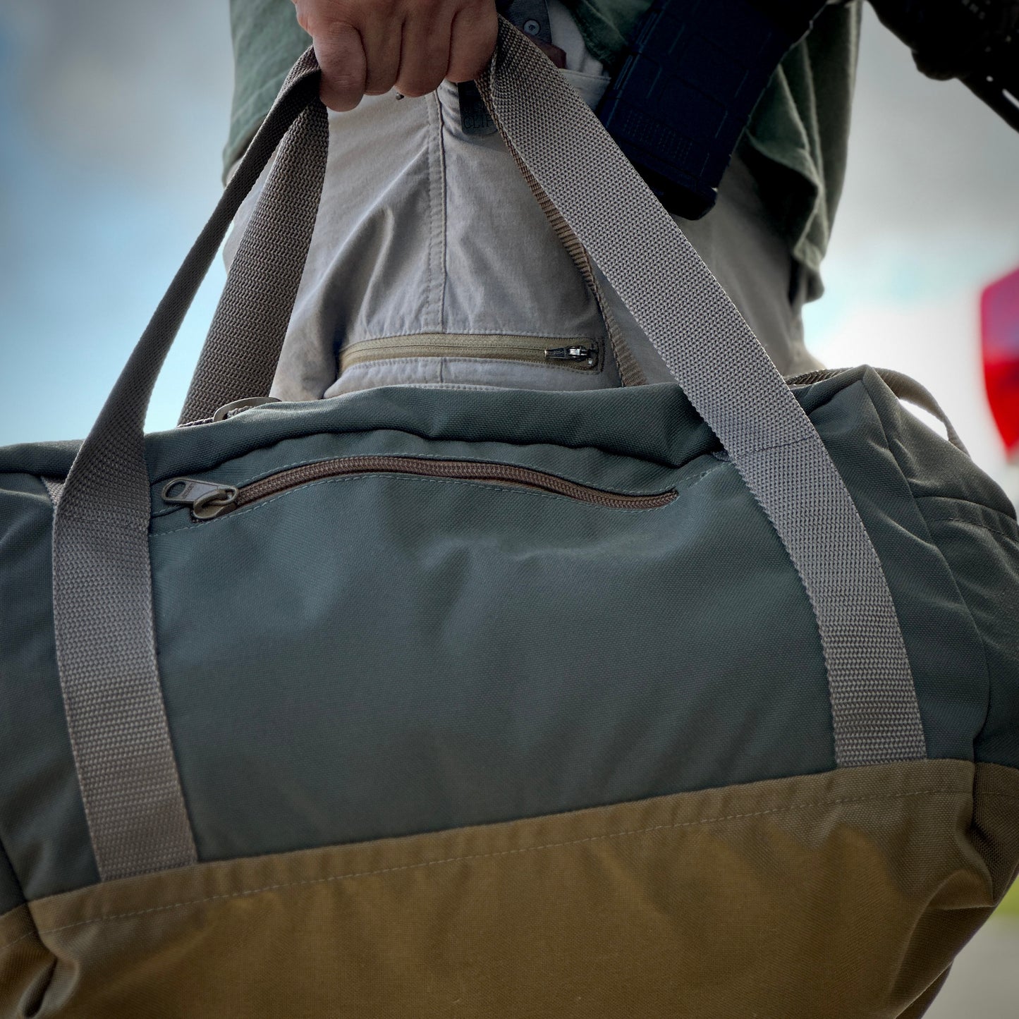 Person holding a stylish duffel bag with a side zipper pocket, ideal for travel and outdoor adventures.